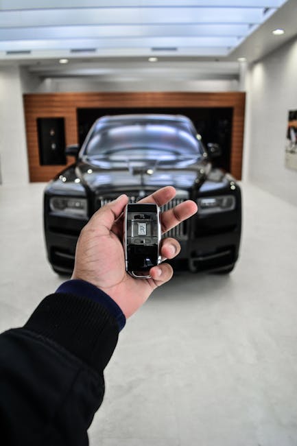 Hand holding a luxury car key with sleek vehicle in background. Perfect for transportation themes.